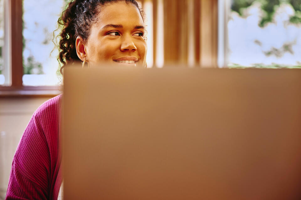 female, in a purple top, smiling, looking away with a laptop in front of her
