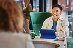 Male smiling, sitting on a table behind his tablet