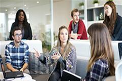 an image of a team sitting on chairs and some standing while discussing something